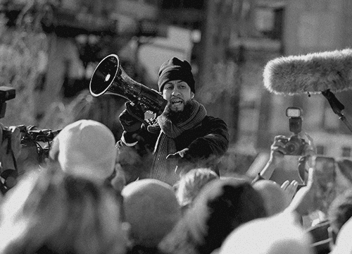 Person talking through mega phone to a crowd for the he gets us agenda page